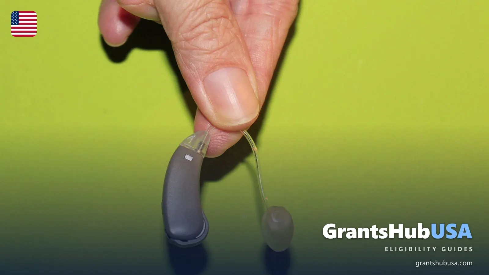 Hand holding a small behind-the-ear hearing aid, illustrating whether Medicare covers hearing aids in 2026. GrantsHubUSA Medicare guide.