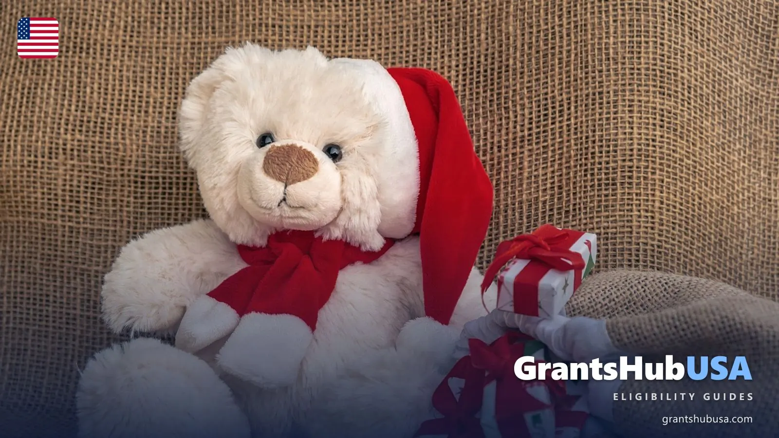 A white teddy bear in a red Santa hat and scarf sits beside small gifts wrapped in red ribbon, the kind of new toy families request through a local holiday toy program.