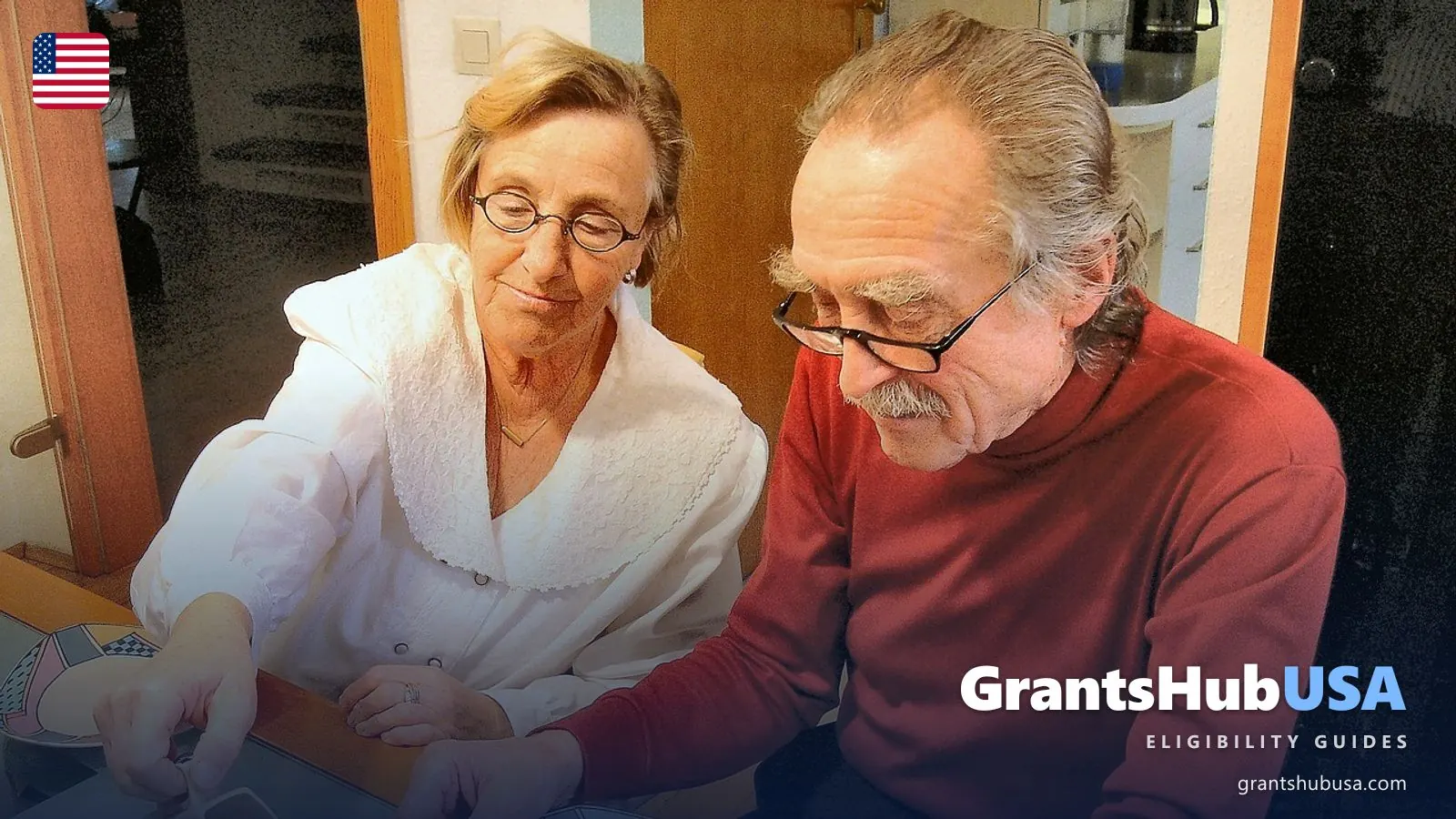 An older couple sitting side by side at their kitchen table, looking down at something together